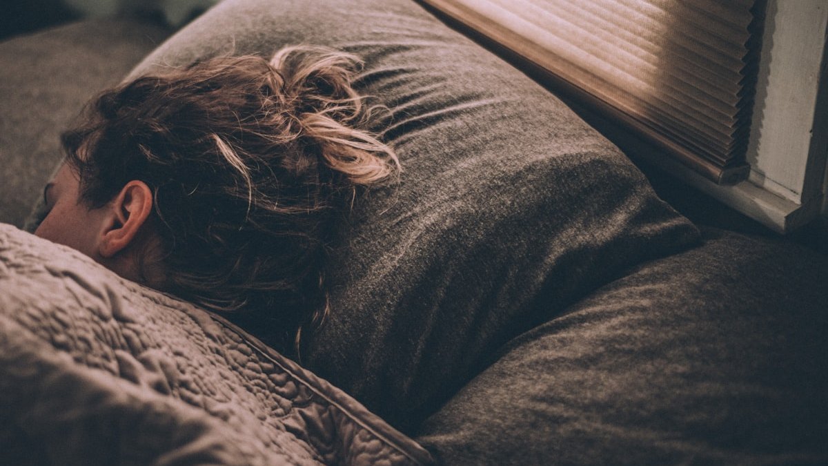 Woman sleeping on bed under blankets. — a Sleep Finally guide to Thermostat Settings for Sleep: A Seasonal Guide.