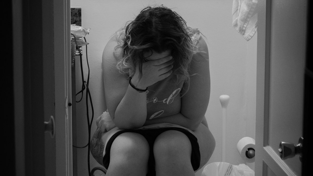 Woman in white tank top sitting on toilet bowl. — a Sleep Finally guide to Waking Up to Pee: When Is It a Problem.