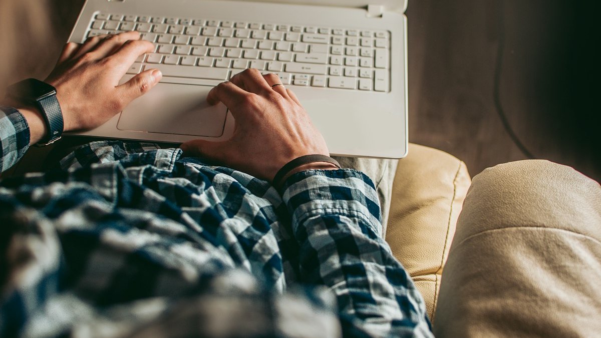 A man laying on a couch using a laptop computer. — a Sleep Finally guide to What Happens When You Skip Your Wind-Down for a Week.