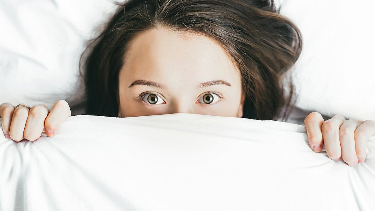 Woman covering her face with blanket. — a Sleep Finally guide to What Is Social Jet Lag? The Weekly Flight You Never Booked.