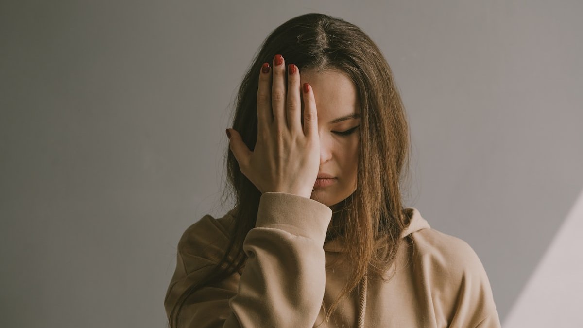 A woman covering her face with her hands. — a Sleep Finally guide to When Night Sweats Are More Than Menopause.
