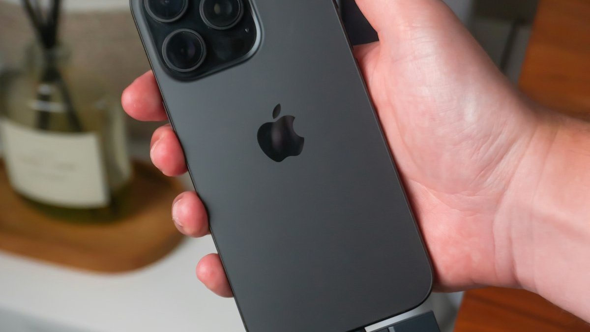 Hand holding a dark gray smartphone with apple logo. — a Sleep Finally guide to Where to Dock Your Phone at Night.