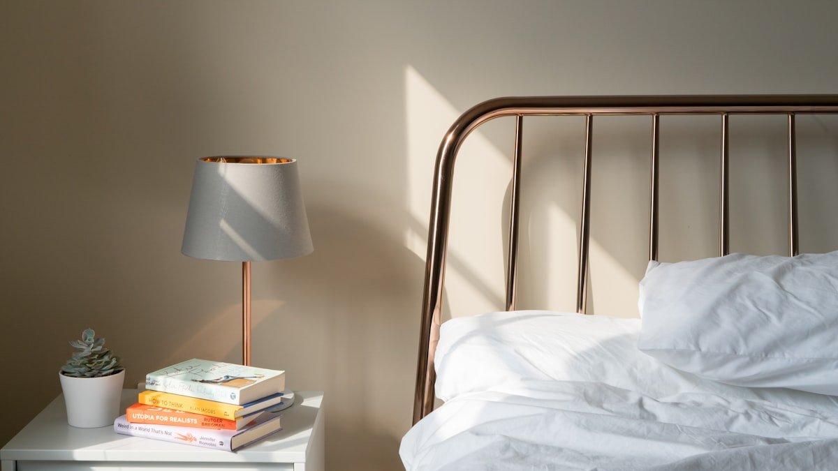Table lamp on white wooden nightstand beside bed. — a Sleep Finally guide to Why 65 to 68 Degrees Is the Sleep Sweet Spot.