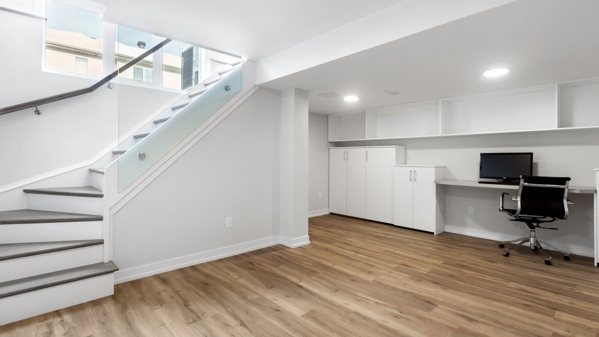 An empty room with a desk, computer, and stairs. — a Sleep Finally guide to Why Bill's Basement Office Wrecked His Sleep.