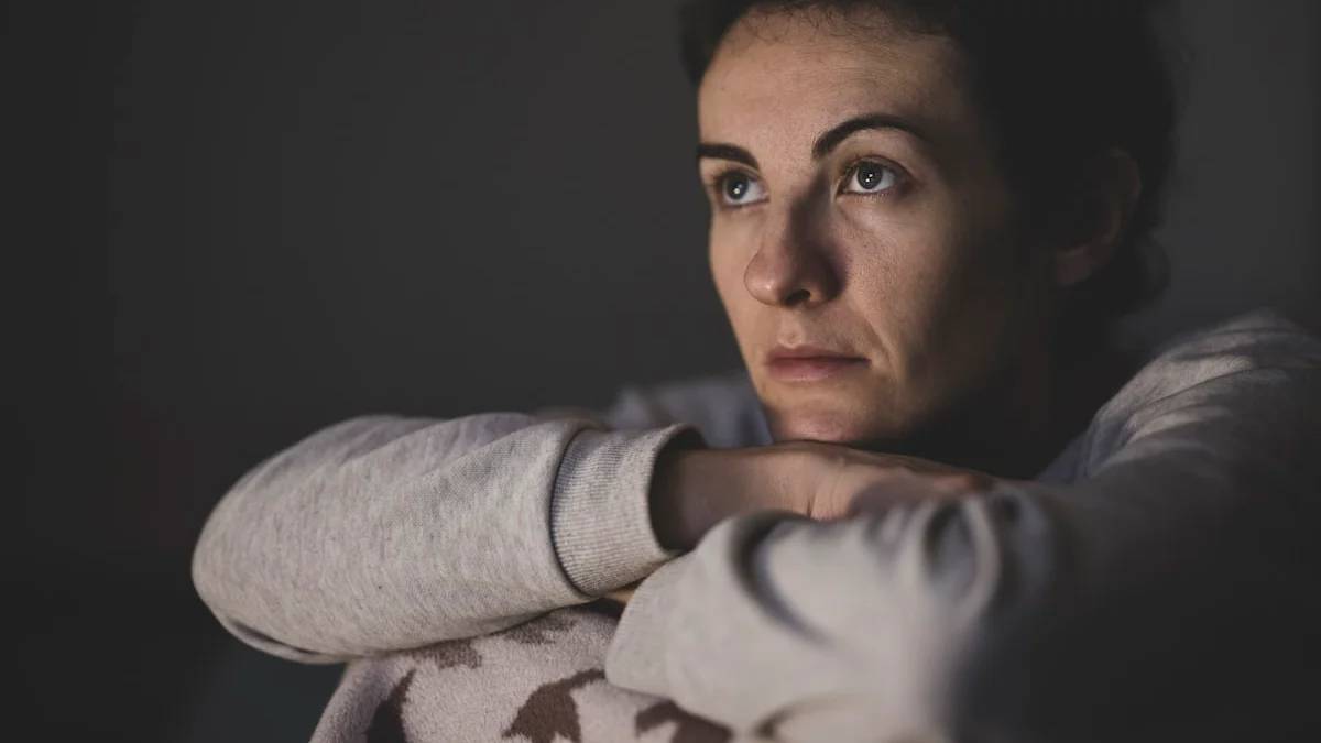 A woman with dark hair resting her chin on her hands in dim light — a Sleep, Finally guide to Why Perimenopause Wakes You at 3 AM