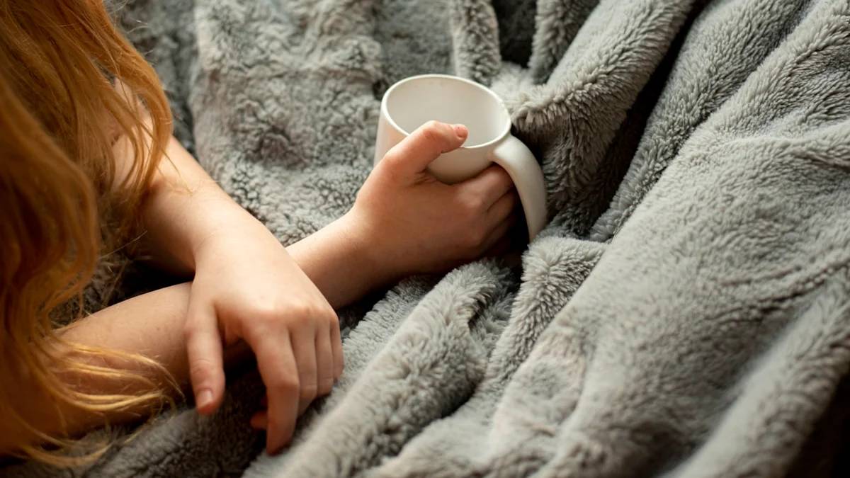 woman holding white ceramic mug — a Sleep, Finally guide to Why You Wake Up Cold at 3am